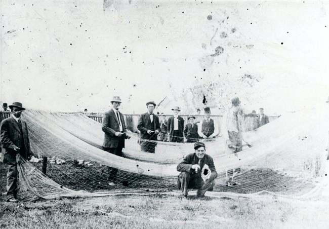 Black and white photo of men standing with fishing nets.