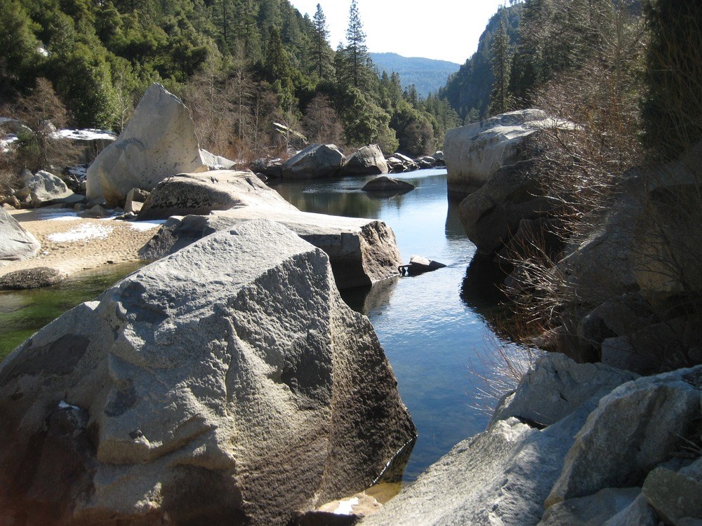 Merced River A view through boulders of the Merced River with mountains in the boackground.