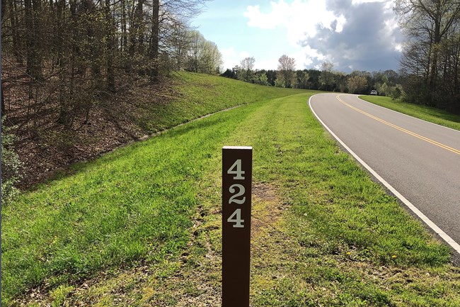 A brown post with white number 424, a tree lined road, blue sky.