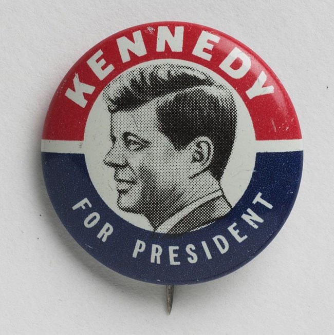 Red, white and blue Kennedy for President campaign button with black and white profile of John F. Kennedy in center.