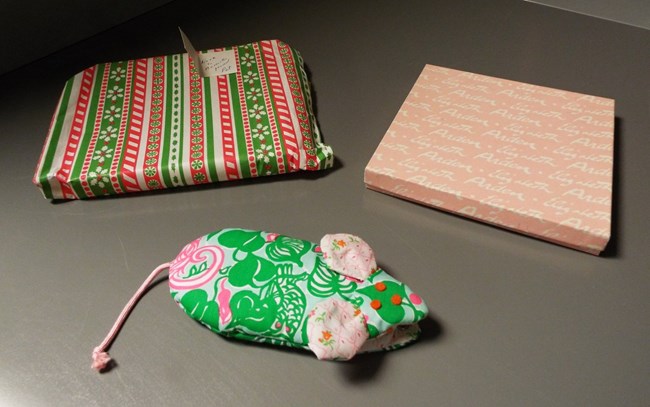 A colorful fabric mouse-shaped eyeglass case sits next to two boxes with colorful wrapping paper