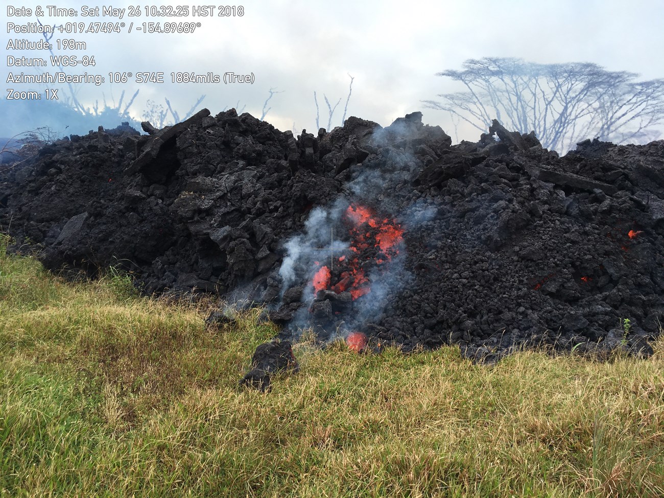 Photo of a blocky lava flow advancing into a grassy meadow.