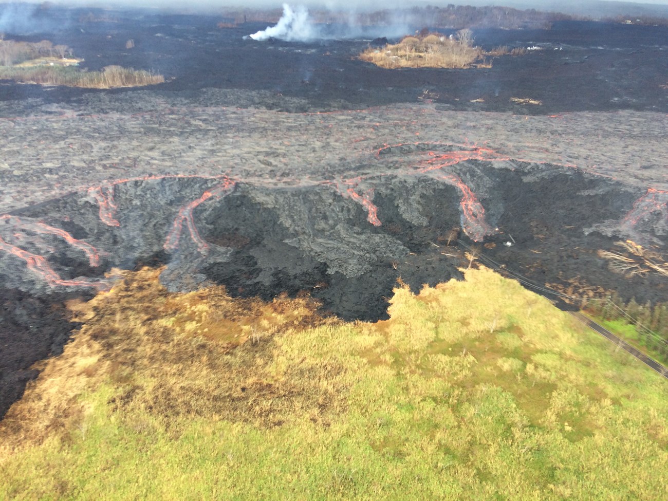 photo of a volcanic landscape with active lava flows and a steaming vent in the distance
