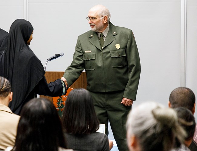 Regional Director Bert Frost shakes hands with one of the new citizens at the ceremony. Regional director Bert Frost (right) shakes the hand of a young woman in a black abaya.