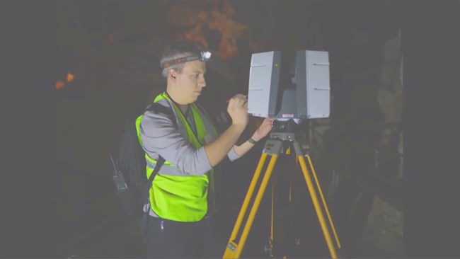 Dr. Williamson uses a stylus while scanning Carlsbad Caverns, wearing a headlamp, backpack, and safety gear.