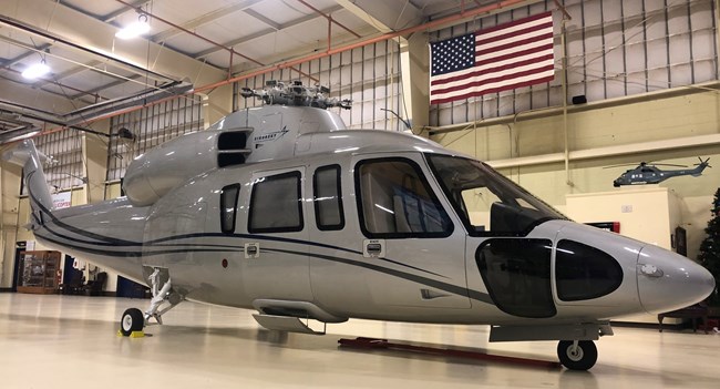 A gray business helicopter painted gray in a hangar under an American flag.
