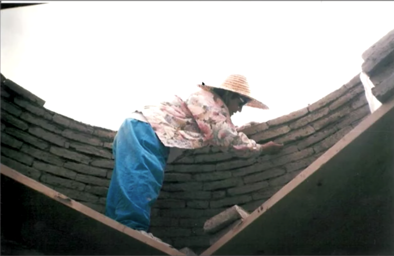 Woman working on an curved adobe wall.