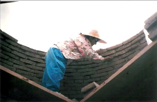 Sister Cita Jimenez, master vault mason. Woman working on an curved adobe wall.