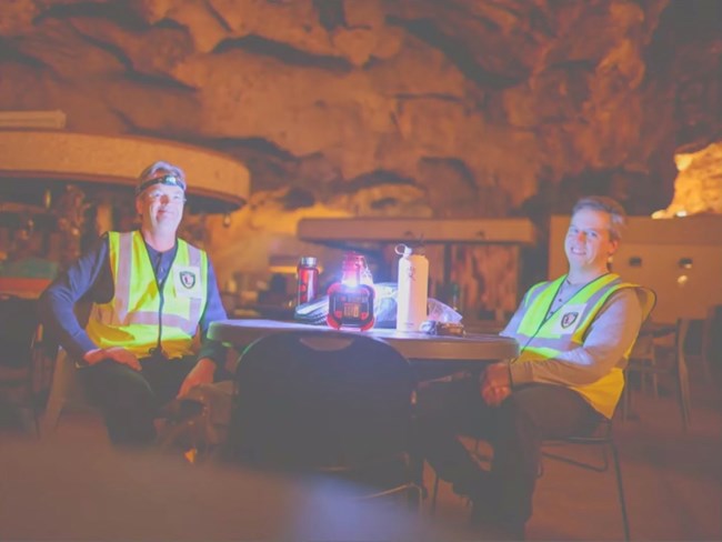 Two scanning crew members take a break at a folding table and chairs in the cavern.