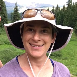 A headshot of Rachel Adler in the field with a backdrop of forest.