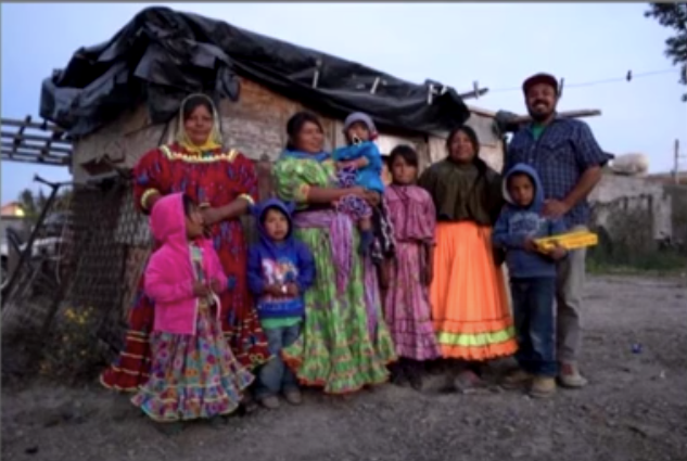 Tarahumara family standing in front of an adobe house with Sandro Canovas.