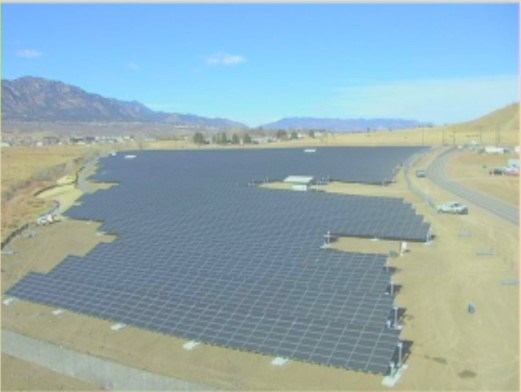 Fort Carson solar project in 2009. A solar array bordered by trees, roads, and an arroyo. Mountains lie in the distance.