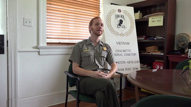 Nathan Hall sits with a memorial sign behind him honoring Vietnam veterans who are also buried at Chalmette National Cemetery.