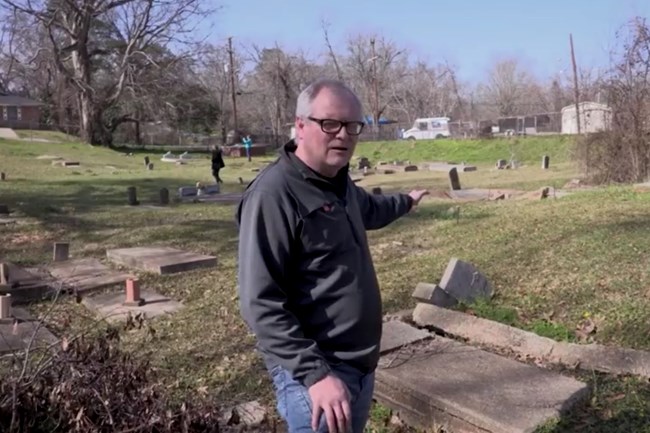 Simeon Warren points behind to collapsed concrete tombs, sinkholes, and metal poles.