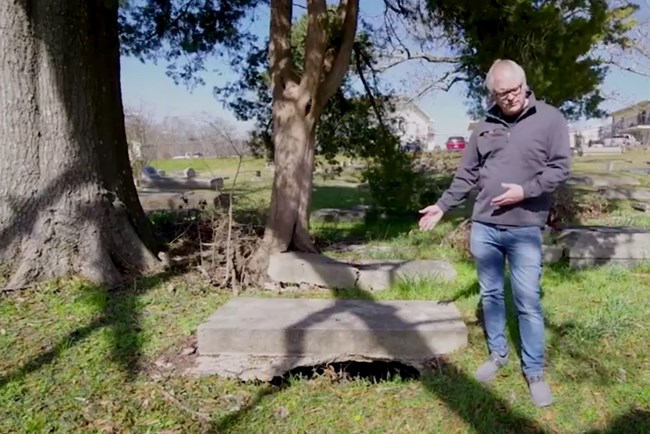 Simeon Warren points out open earth beneath a grave slab, which can be a safety problem as eroded earth falls away.