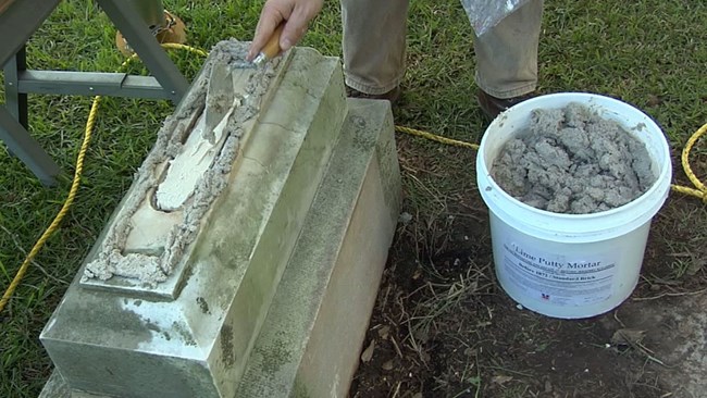Jason Church applies new mortar to the cleaned base of a headstone.