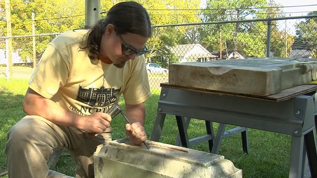 Jason Church uses a chisel and hammer to remove old mortar from the base of a grave stone.