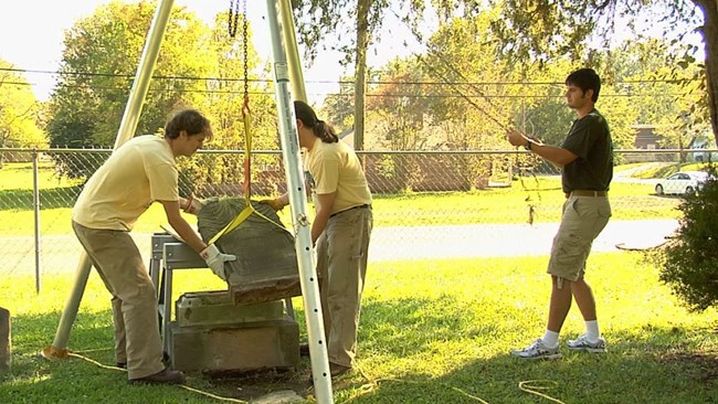 Jason Church and two research associates use a tripod hoist while resetting a gravestone.