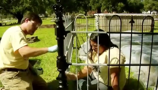 Jason Church and Bianca Garcia hand-paint the repaired iron fence.