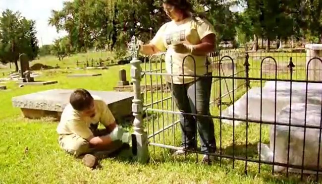 It is recommended that all primer and paint be applied by brush to prevent over spray and staining in the cemetery. Jason Church and Bianca Garcia apply primer to the cleaned, dried, repaired iron fence.