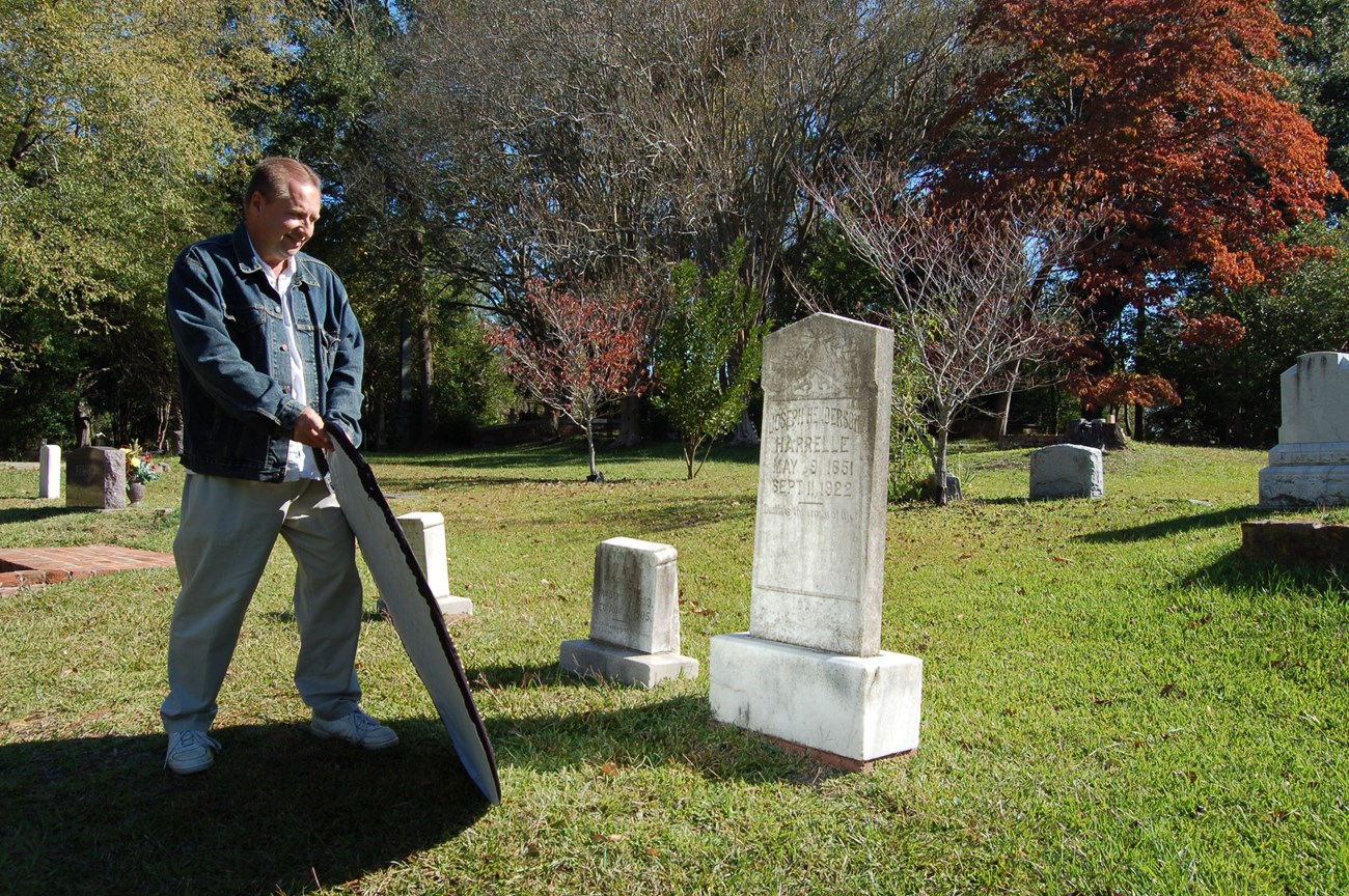 A car sun shade or photographer’s reflector can be used to bounce light on to the stone from an angle. Raking light can assist in making a carving more legible. NCPTT research assistant Curtis Desselles uses a reflector to photograph a worn inscription.