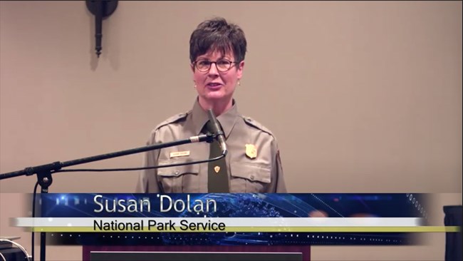 Photo of the presenter in a NPS uniform speaking at a lectern.