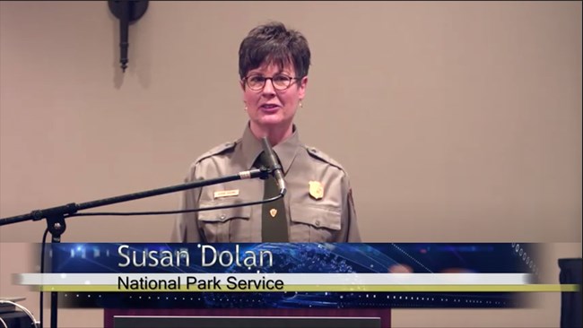 Susan Dolan, National Park Service. Photo of the presenter in a NPS uniform speaking at a lectern.