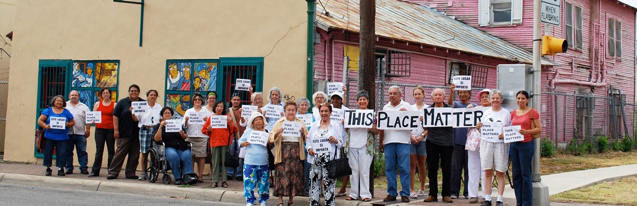 Community members stand in front of the museum with "this place matters" signs.