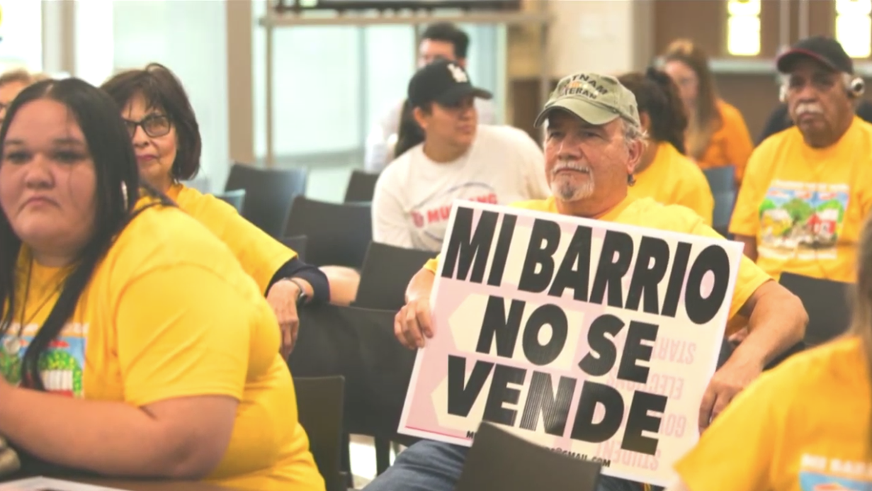 ¡Mi barrio no se vende! a sign says among a group of Latinx residents.