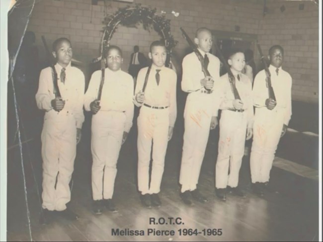 A rifle team of six middle school boys stand at right-shoulder arms.