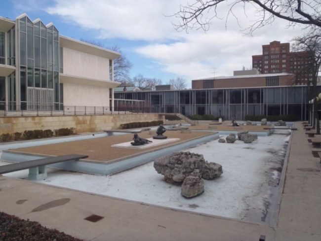 A photo showing a drained reflecting pool with stones, islands, and statuary.