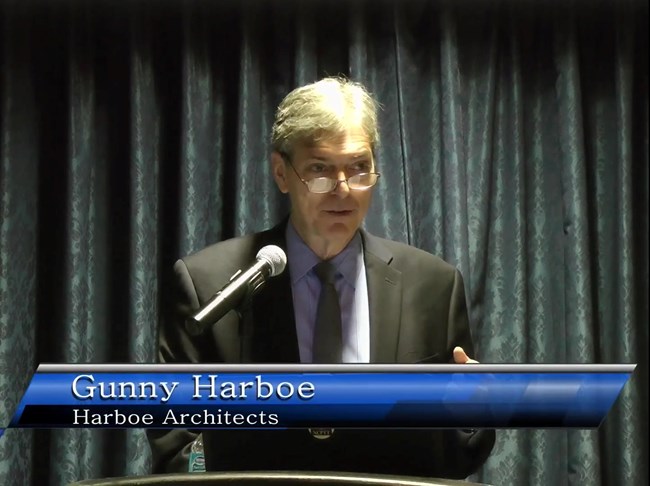 The speaker Gunny Harboe stands at a lectern, presenting.