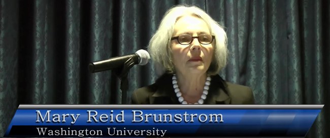 Mary Reid Brunstrom, Washington University, stands at a lectern delivering a presentation.