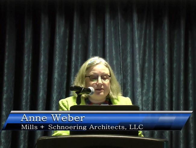 Anne Weber standing at a lectern, presenting.