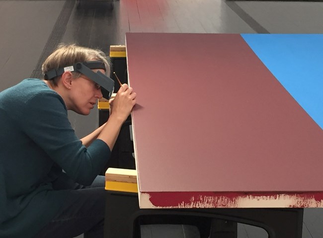 Cory Rogge taking a paint sample. Paint sample being taken from a red colored plywood art piece.