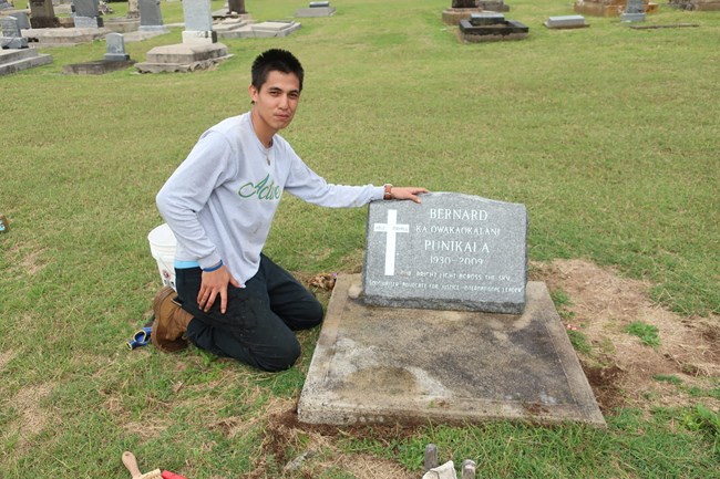 CJ Sweezey with a hand on a gravestone after cleaning.