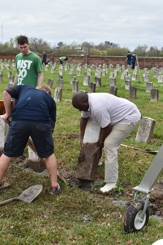 Teddy Pierre lifting a headstone out of the ground before resetting.