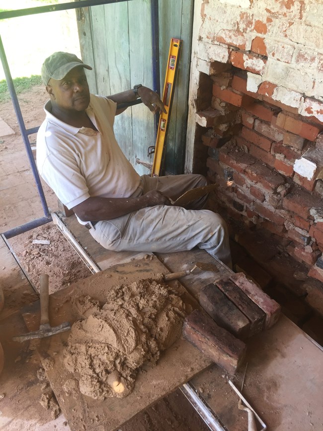 Teddy Pierre pausing briefly for a photograph as he examines a historic masonry wall.