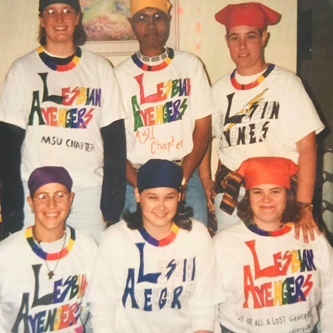 Six women in handmade rainbow "Lesbian Avengers" tee shirts and rainbow necklaces.