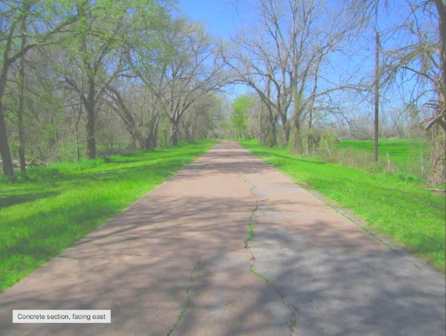 Photo of a narrow concrete slab road heading east through woodland, scrub, and farms.