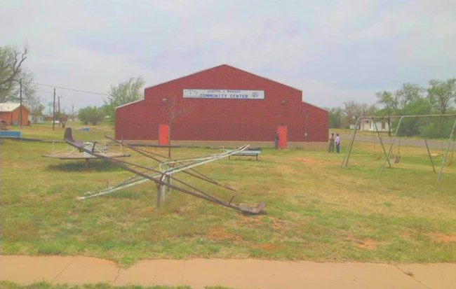 A masonry building gym, now a community center, behind a playground.