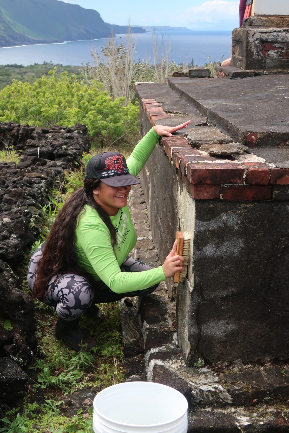 Student Leesaan Kaleikini begins cleaning a large tomb with D/2, the Pacific Ocean in the background.