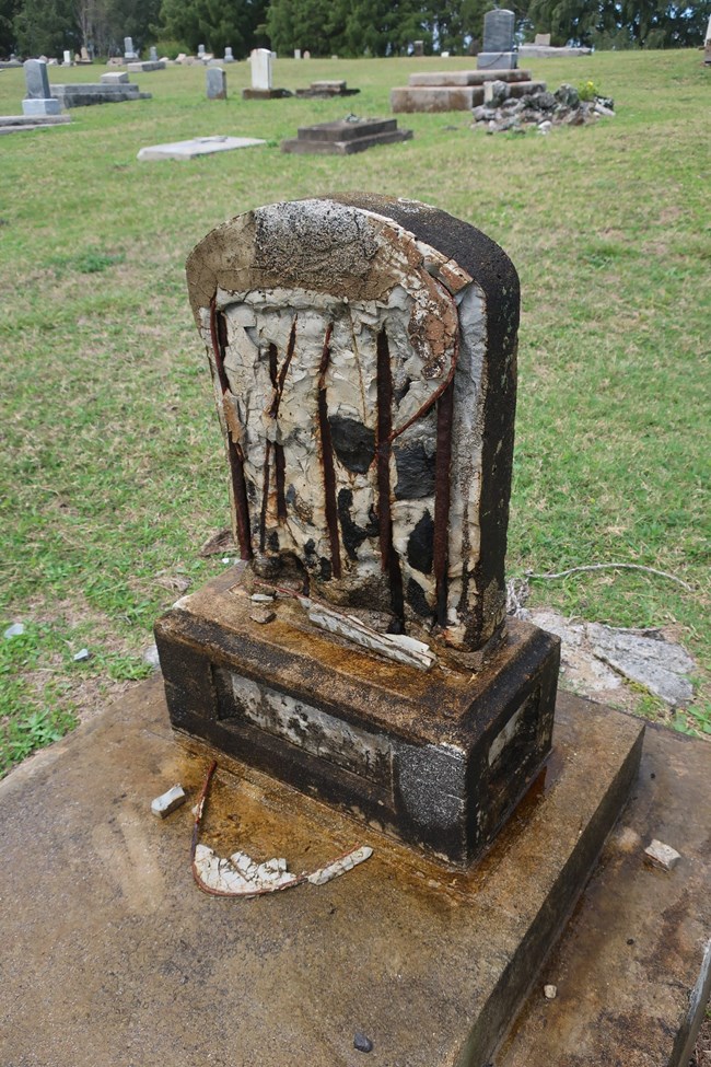 Cast concrete grave marker with failing ferrous reinforcement.