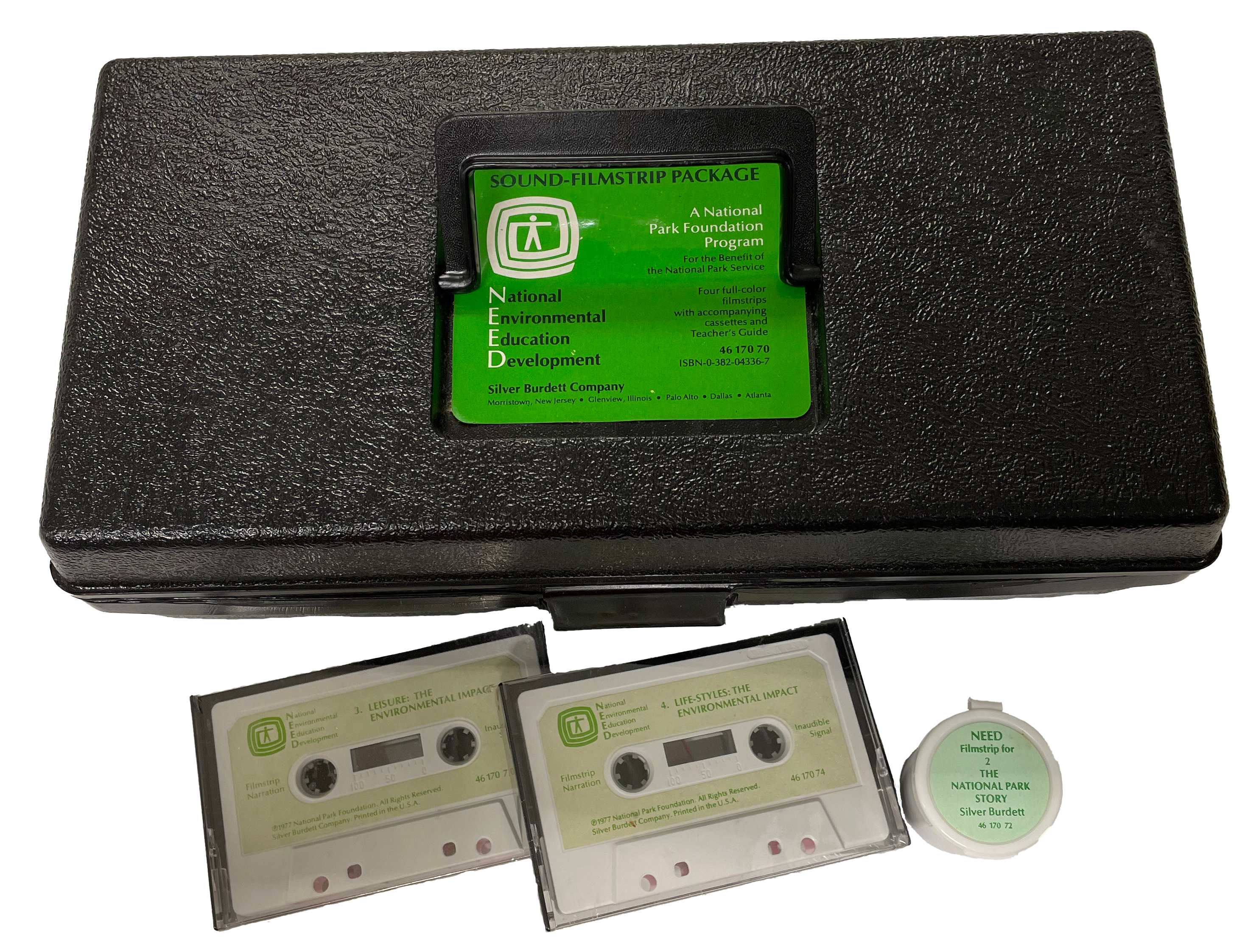 NEED kit Plack plastic box with green label. Two audiocassettes and a filmstrip cannister beside it.