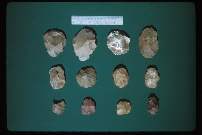 a variety of worked stones and arrowhead-like objects laid out on green cloth.