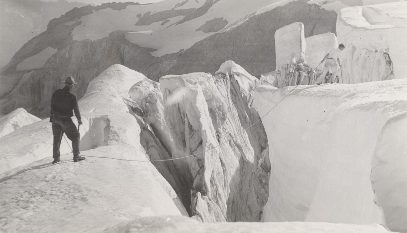 Nisqually Glacier, 1933. Two men stand on opposite sides of a crevasse with a rope across it.