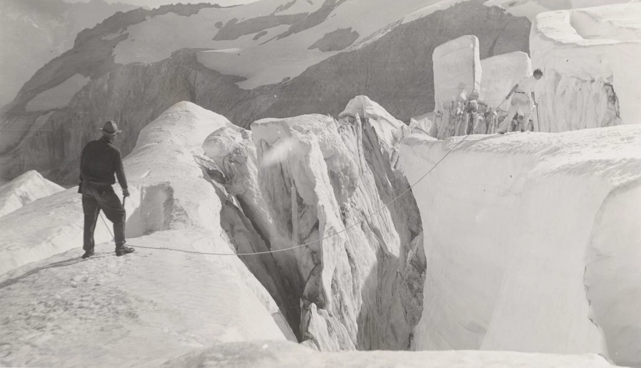 Nisqually Glacier, 1933. Two men stand on opposite sides of a crevasse with a rope across it.