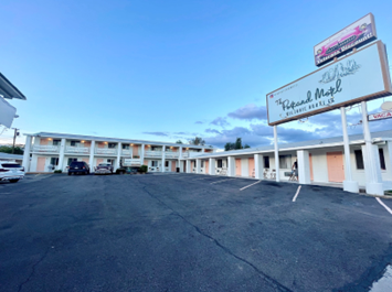 from the parking lot, a one-story, white colored motel building with a wraparound veranda.