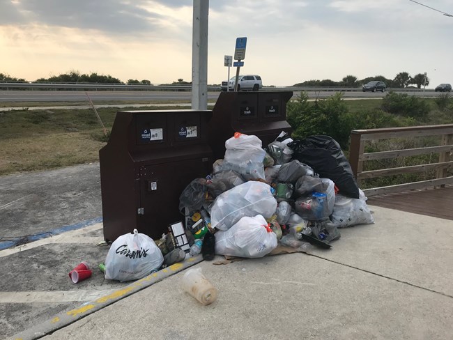 Image of overflowing trash cans in river beach parking lot.