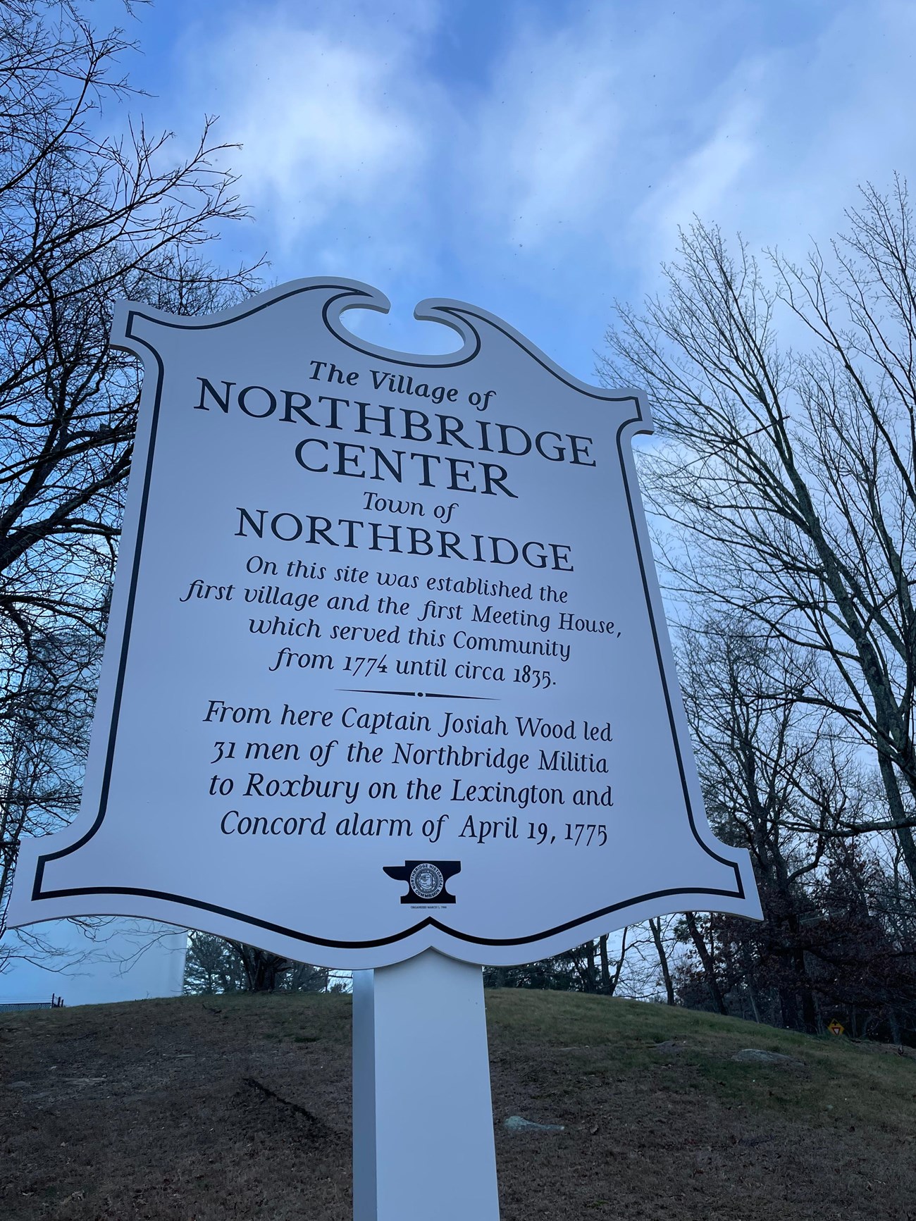 A white sign against a blue sky indicating this was the location of the historic Northbridge meetinghouse